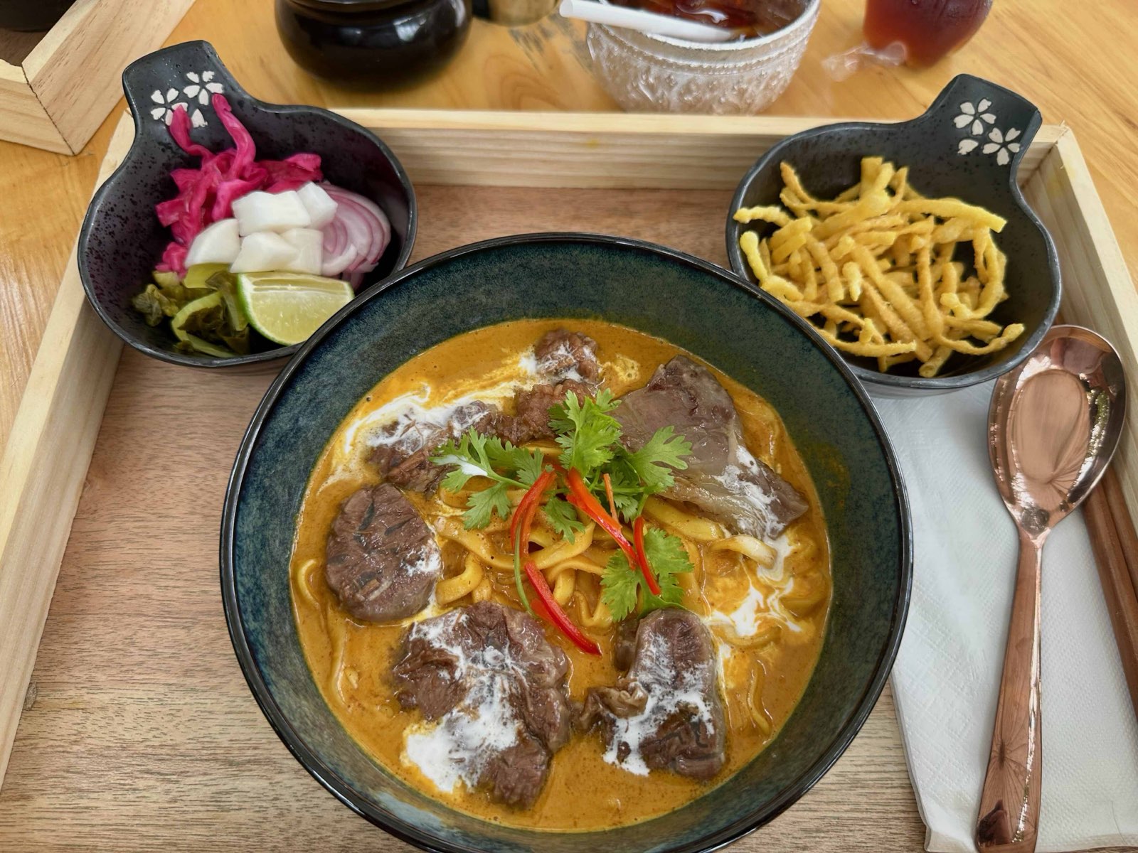 A bowl of khao soi, Chiang Mai's curry noodle soup, with crispy noodles, pickles, shallots and lime on the side